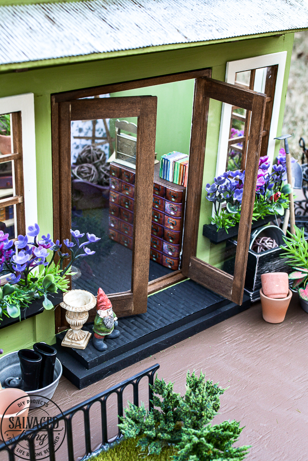 Tour a miniature vintage garden shop dollhouse for great ideas for your own dollhouse decor. See how to make a cozy home, lush garden and outdoor miniature yard! COmplete with garden gnomes, miniature potted plants and sitting areas. #dollhouse #miniatures #DIYdollhouse #vintagegarden #tinydecor