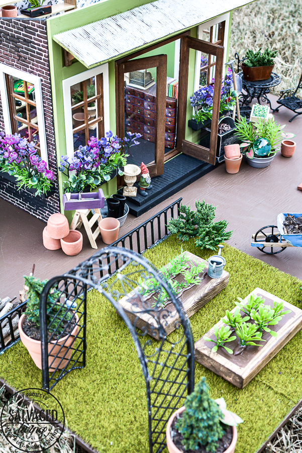 Tour a miniature vintage garden shop dollhouse for great ideas for your own dollhouse decor. See how to make a cozy home, lush garden and outdoor miniature yard! COmplete with garden gnomes, miniature potted plants and sitting areas. #dollhouse #miniatures #DIYdollhouse #vintagegarden #tinydecor