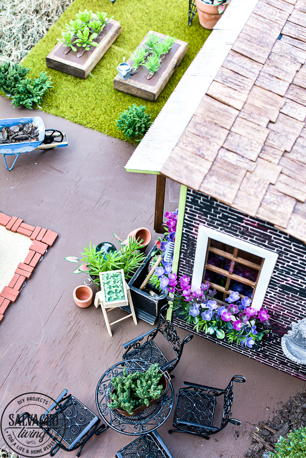 Tour a miniature vintage garden shop dollhouse for great ideas for your own dollhouse decor. See how to make a cozy home, lush garden and outdoor miniature yard! COmplete with garden gnomes, miniature potted plants and sitting areas. #dollhouse #miniatures #DIYdollhouse #vintagegarden #tinydecor