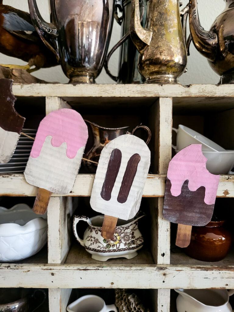 Adorable popsicle decor for your summer decorating enjoyment right here! These no mess popsicles are the perfect way to add some childhood fun to your adult vintage home. Made to look like vintage style signs, these popsicles crafted from cardboard are not only easy and fun to make, but a cheap decor idea! Use your own color shceme to make them fit your decorating style. Would be great 4th of July decor as well! #summerdecor #cardboardcraft #DIYgarland