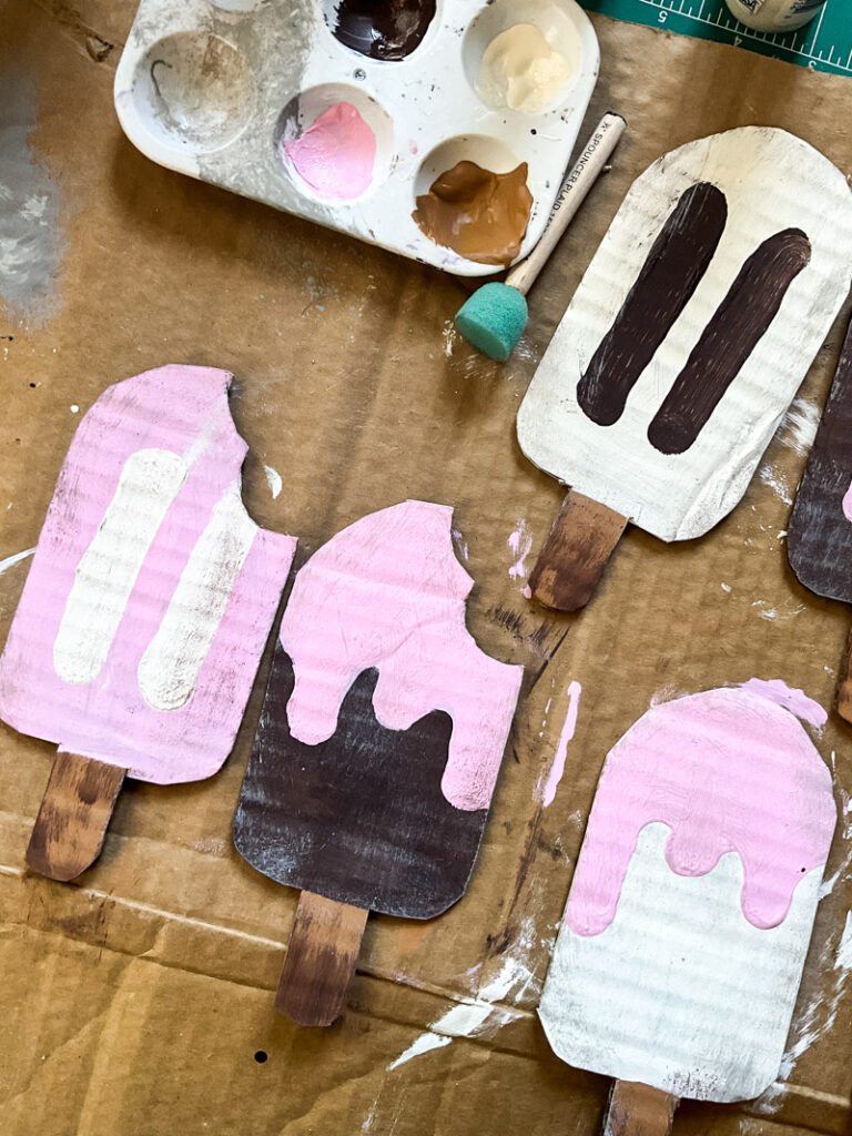 Adorable popsicle decor for your summer decorating enjoyment right here! These no mess popsicles are the perfect way to add some childhood fun to your adult vintage home. Made to look like vintage style signs, these popsicles crafted from cardboard are not only easy and fun to make, but a cheap decor idea! Use your own color shceme to make them fit your decorating style. Would be great 4th of July decor as well! #summerdecor #cardboardcraft #DIYgarland