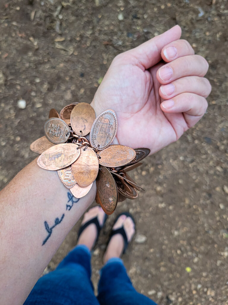 How to make a pressed penny bracelet. This DIY charm bracelet is made from inexpensive collectible souvenirs. FInd the best vacation memory in these pressed penny pieces! Then take them home amd add them to your memory keeping charm bracelet, copper is so beautiful and perfect for reliving favorite vacation spots all while looking uniquely stylish! This is an easy DIY jewelry project that has a ton of meaning. #charmbraceletDIY #pressedpennyidea #pennydisplay #souvenircollection #travelmemory