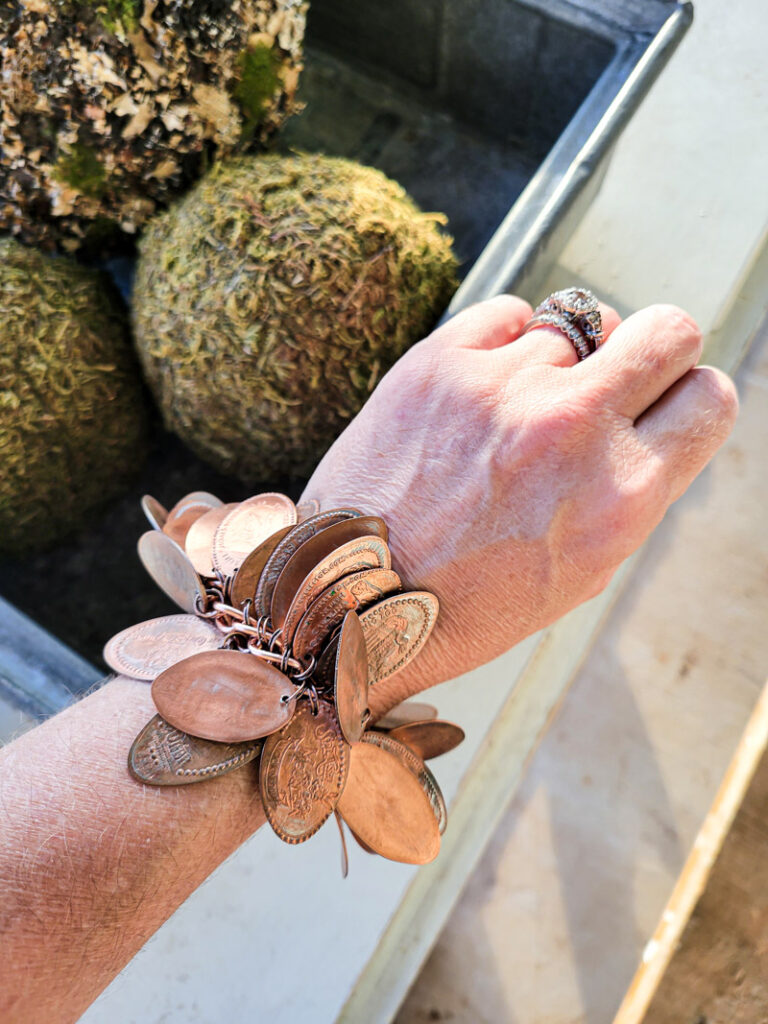 How to make a pressed penny bracelet. This DIY charm bracelet is made from inexpensive collectible souvenirs. FInd the best vacation memory in these pressed penny pieces! Then take them home amd add them to your memory keeping charm bracelet, copper is so beautiful and perfect for reliving favorite vacation spots all while looking uniquely stylish! This is an easy DIY jewelry project that has a ton of meaning. #charmbraceletDIY #pressedpennyidea #pennydisplay