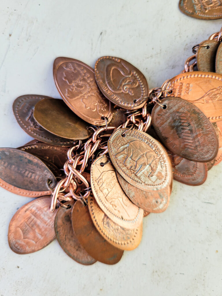 How to make a pressed penny bracelet. This DIY charm bracelet is made from inexpensive collectible souvenirs. FInd the best vacation memory in these pressed penny pieces! Then take them home amd add them to your memory keeping charm bracelet, copper is so beautiful and perfect for reliving favorite vacation spots all while looking uniquely stylish! This is an easy DIY jewelry project that has a ton of meaning. #charmbraceletDIY #pressedpennyidea #pennydisplay